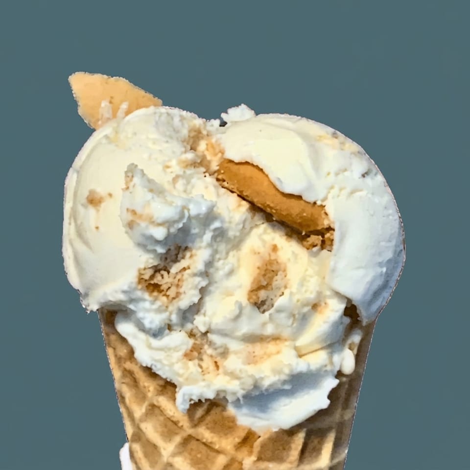 Waffle cone filled with scoops of creamy vanilla ice cream and cookie pieces against a dark teal background.